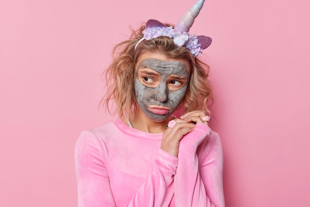 Unhappy frustrated woman with hairstyle looks sadly away wears unicorn headband casual jumper undergoes beauty treatments poses against pink background prepares for party wants to look beautiful