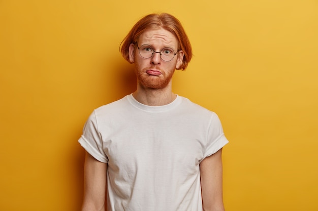 Unhappy gloomy guy hipster with ginger hair, thick beard, purses lower lip