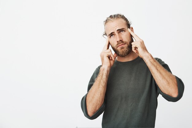 Unhappy handsome man with good hairstyle and beard feeling extremely tired, holding finger on forehead