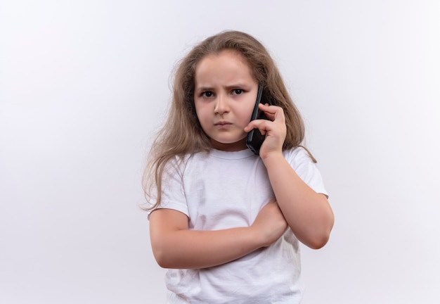 孤立した白い壁に電話で白いTシャツスピーカーを身に着けている不幸な小さな女子高生