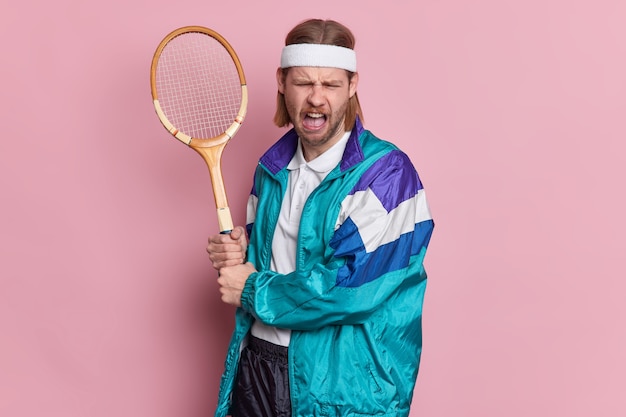 불행한 남자 테니스 선수는 경쟁을 잃기 위해 라켓을 화나게하고 스포츠웨어를 입은 불쾌한 찡그린 얼굴을합니다.
