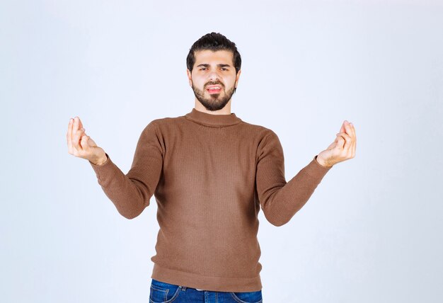 Unhappy man standing and posing with hands on white wall. 