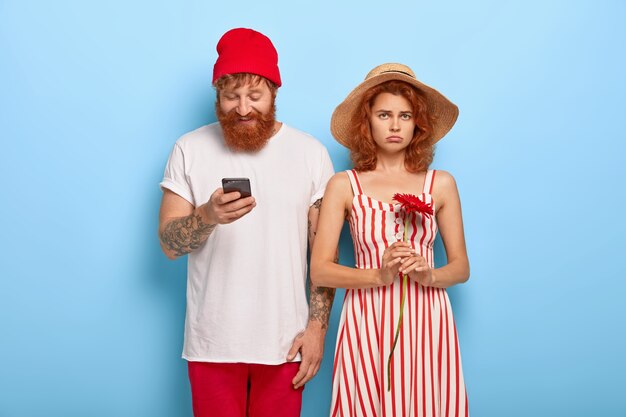 불행한 빨강 머리 여자는 남자 친구가 휴대 전화를 사용하는 동안 지루해집니다.