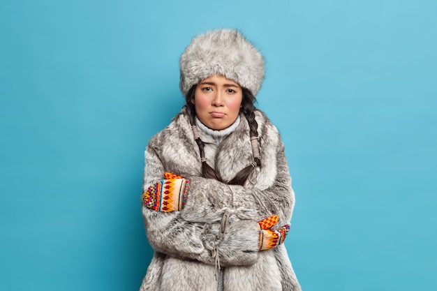 Unhappy scandinavian woman in fur hat and coat crosses hands and feels freezing trembles during severe frosty day wears winter outerwear