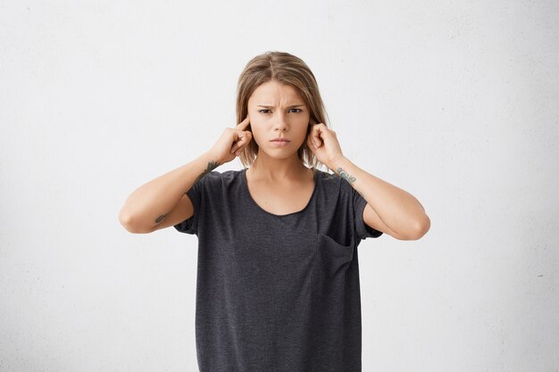 Unhappy stressed out teenage girl plugging ears with fingers doesn't want to hear annoying noise or ignoring stressful and unpleasant situation or conflict.