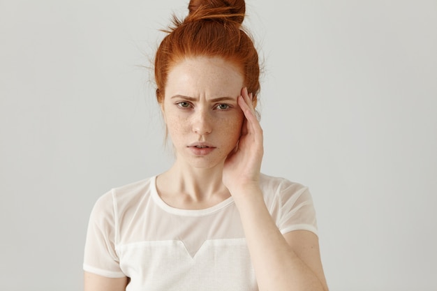 Foto gratuita giovane donna rossa stressata infelice con la faccia commovente del nodo dei capelli mentre soffre dal forte mal di testa, aggrottando le sopracciglia e guardando con espressione tesa e dolorosa sul suo viso. linguaggio del corpo