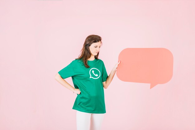 Unhappy woman holding empty orange speech bubble on pink background