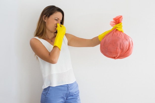 Unhappy woman holding trash with disgusting smell