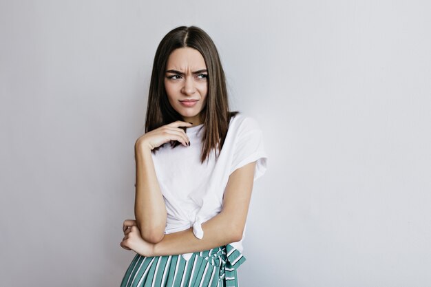 Unhappy woman looking away while posing. Indoor shot of brown-haired female model standing in trendy outfit.