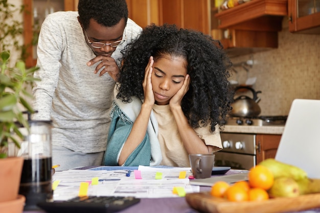 불행한 젊은 아프리카 인은 집에서 청구서를 계산하는 동안 스트레스와 우울해 보일 수 있습니다.