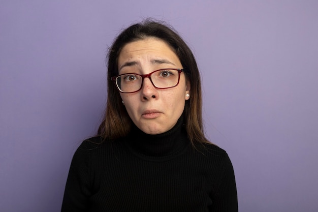 Unhappy young beautiful girl in a black turtleneck and glasses with sad expression 