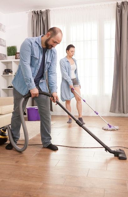 Unhappy young couple cleaning living room floor