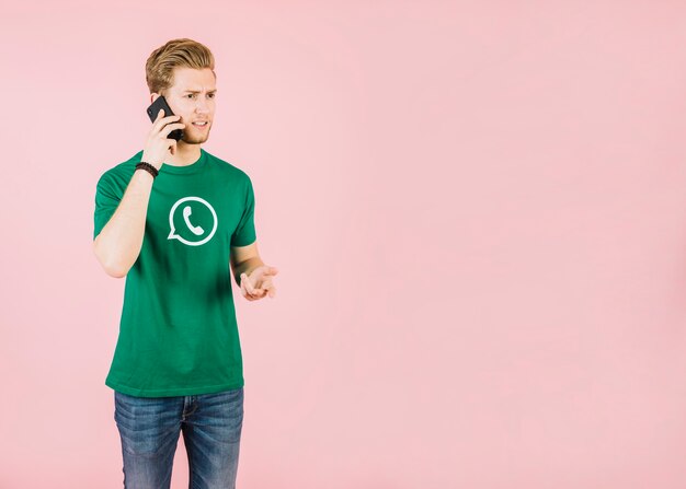 unhappy young man talking on cellphone against pink background