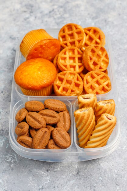 クッキー、waffles.muffins、コンクリート表面の不健康なランチボックス