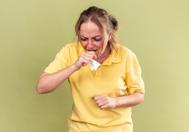 黄色いシャツを着た不健康な女性がインフルエンザと風邪に苦しんで熱咳をしてひどい気分になります