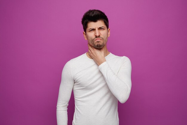 Unhealthy young handsome man looking at camera having sore throat on purple background