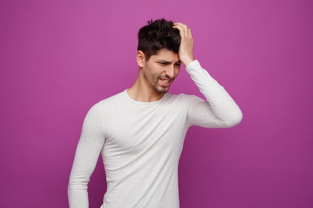 Unhealthy young handsome man looking down keeping hand on head having headache on purple background