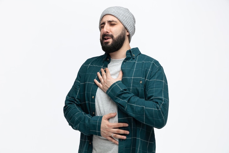 Free Photo unhealthy young man wearing winter hat keeping hands on chest and on belly feeling pain with closed eyes isolated on white background