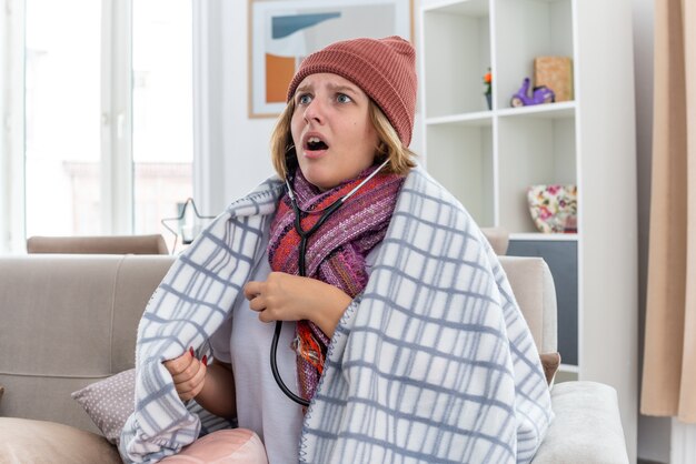 毛布に包まれた暖かい帽子をかぶった不健康な若い女性は、風邪に苦しんで体調を崩し、病気に見えます