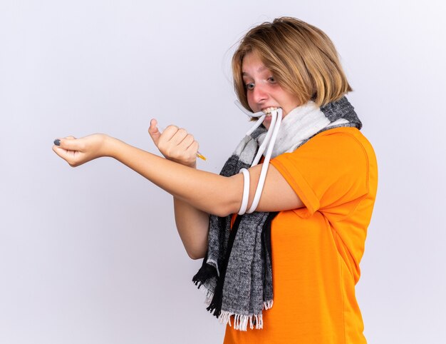 Нездоровая молодая женщина с теплым шарфом на шее чувствует себя больной, страдает от простуды и гриппа, делает себе инъекцию, выглядит обеспокоенной