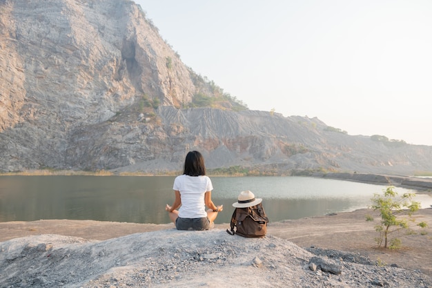 自然との一体感。湖の近くで屋外で瞑想をしている若い女性