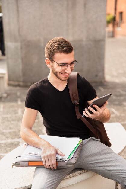 University student sitting on a bench and smiling at tablet