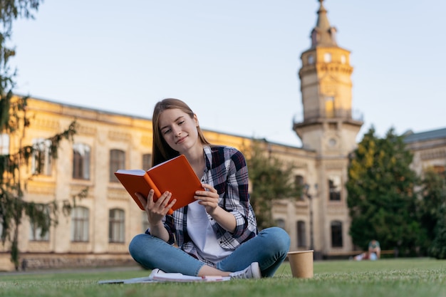 University student studying, reading a book, learning language, exam preparation, sitting on grass, education concept