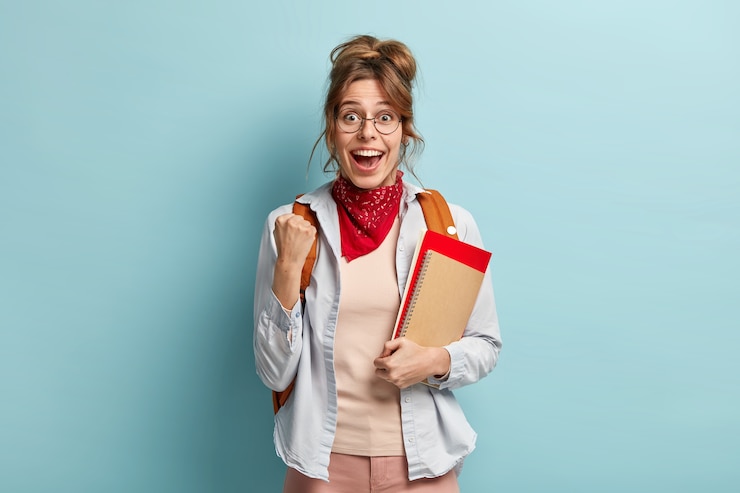 Free Photo university student with glad expression, raises clenched fist, celebrates successfully passed exam, receieves excellent mark