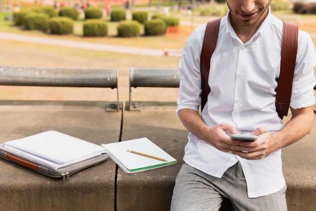 University student working on phone with notebooks next to him