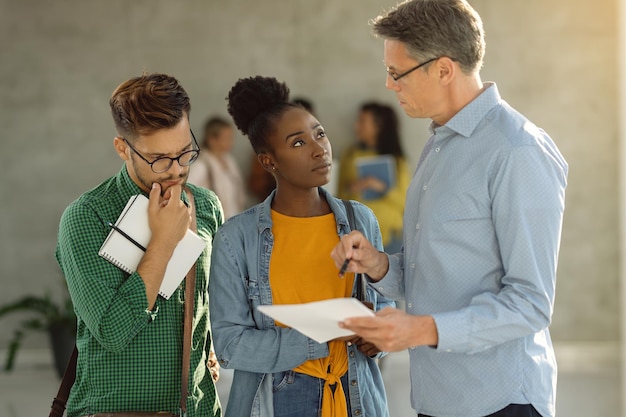 Free photo university students consulting with their professor while standing in a hallway