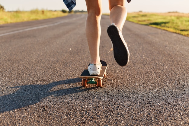 흰색 운동화를 신고 아스팔트 도로에서 스케이트보드를 타는 알 수 없는 사람, 거리에서 스케이트보드를 타는 젊은 여성.