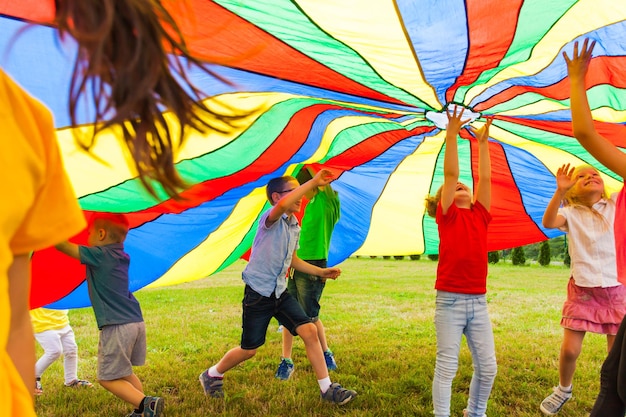 Неограниченное детское веселье под большим радужным парашютом. дети весело бегают под навесом из радуги