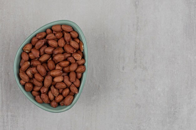 Unpeeled organic peanuts in blue bowl.