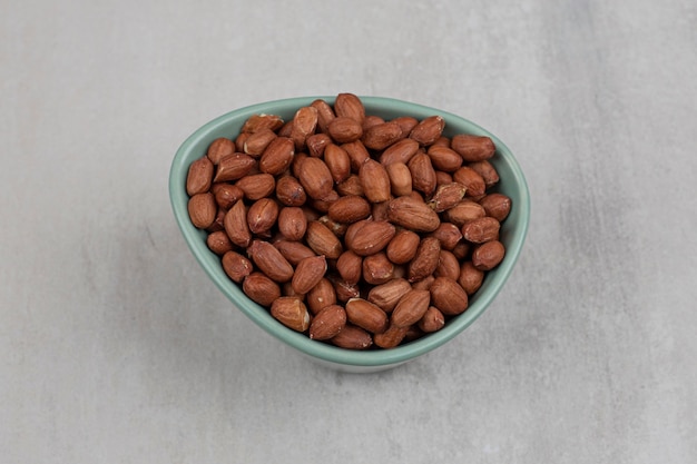 Unpeeled organic peanuts in blue bowl.