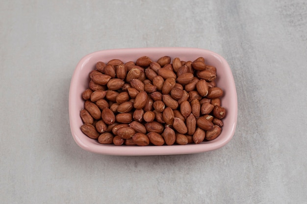 Unpeeled organic peanuts in pink bowl.