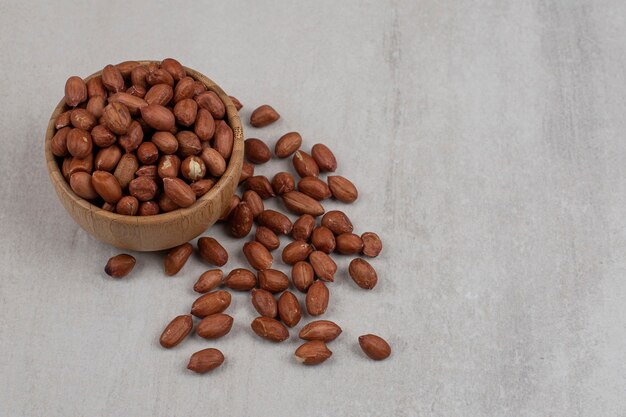 Unpeeled organic peanuts in wooden bowl.