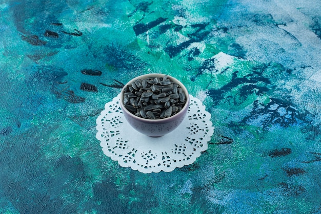 Unpeeled sunflower seeds in bowls on coaster , on the blue table.