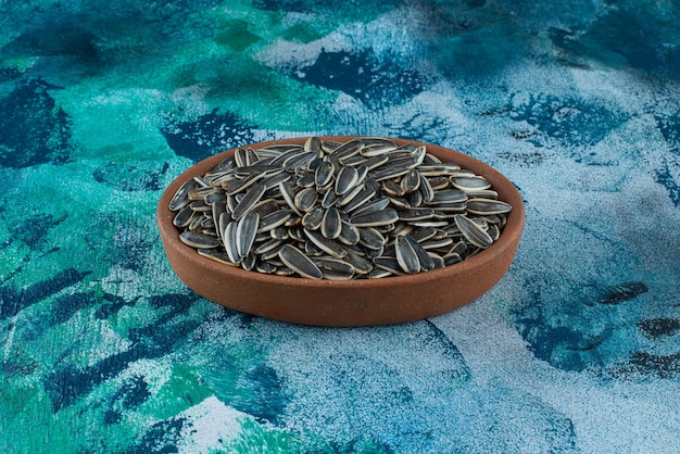 Unpeeled sunflower seeds in a clay bowl, on the marble table.