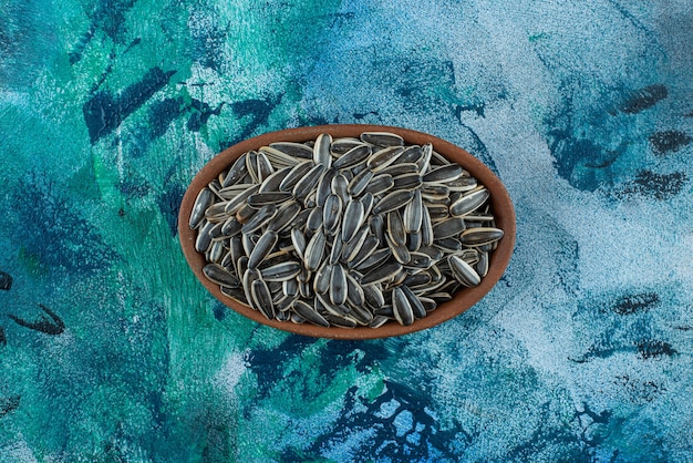 Unpeeled sunflower seeds in a clay bowl, on the marble table.