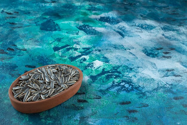 Unpeeled sunflower seeds in a clay bowl, on the marble table.