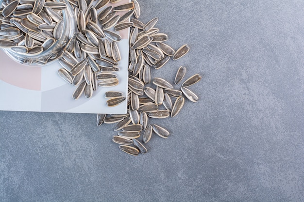 Unpeeled sunflower seeds in glass on notebook, on the marble surface