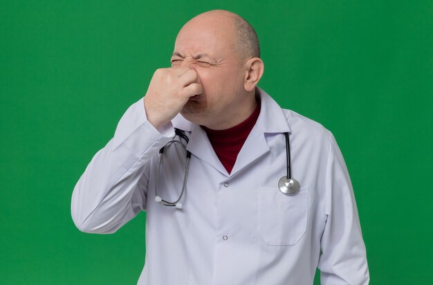 Uomo adulto scontento in uniforme da medico con uno stetoscopio che si chiude il naso