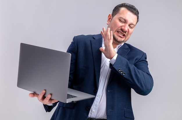 Unpleased adult slavic businessman holding and looking at laptop 