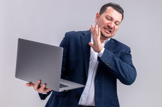 Unpleased adult slavic businessman holding and looking at laptop 