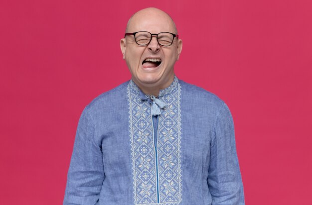 Unpleased adult slavic man in blue shirt wearing optical glasses standing with closed eyes