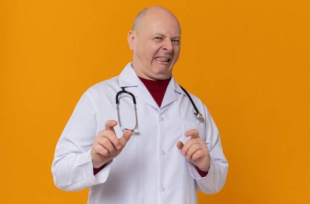 Unpleased adult slavic man in doctor uniform with stethoscope keeping hands open and looking 