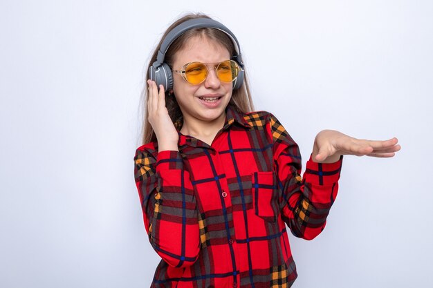 Unpleased beautiful little girl wearing red shirt and glasses with headphones