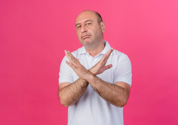 Unpleased casual mature businessman keeping hands crossed doing no gesture isolated on pink background with copy space