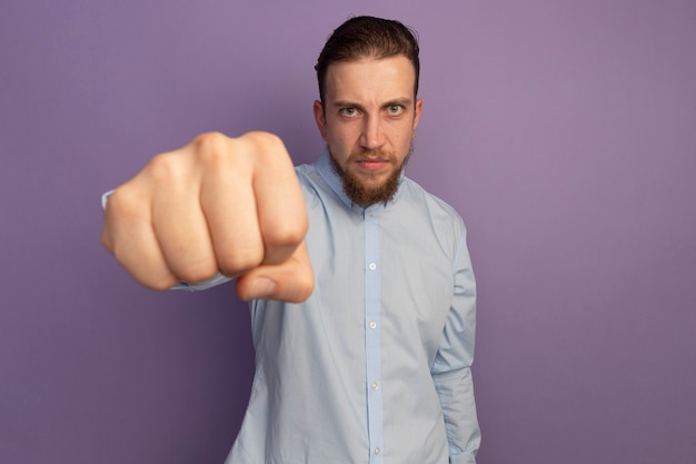 Unpleased handsome blonde man holds fist out isolated on purple wall