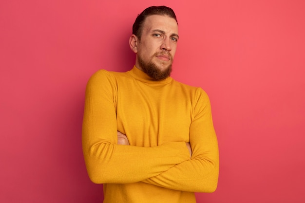 Unpleased handsome blonde man stands with crossed arms on pink